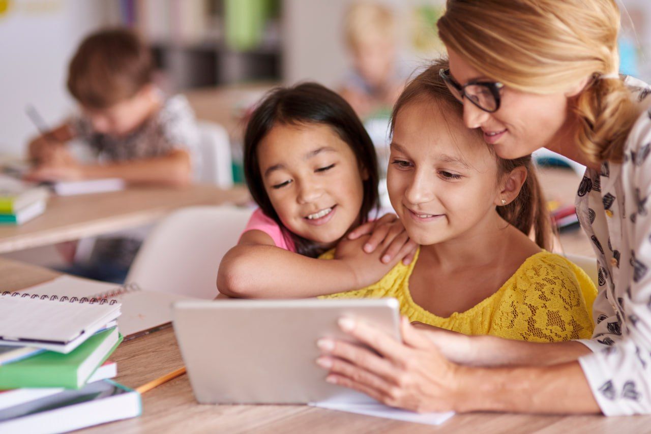 Teacher assisting students using a digital school app on a tablet.