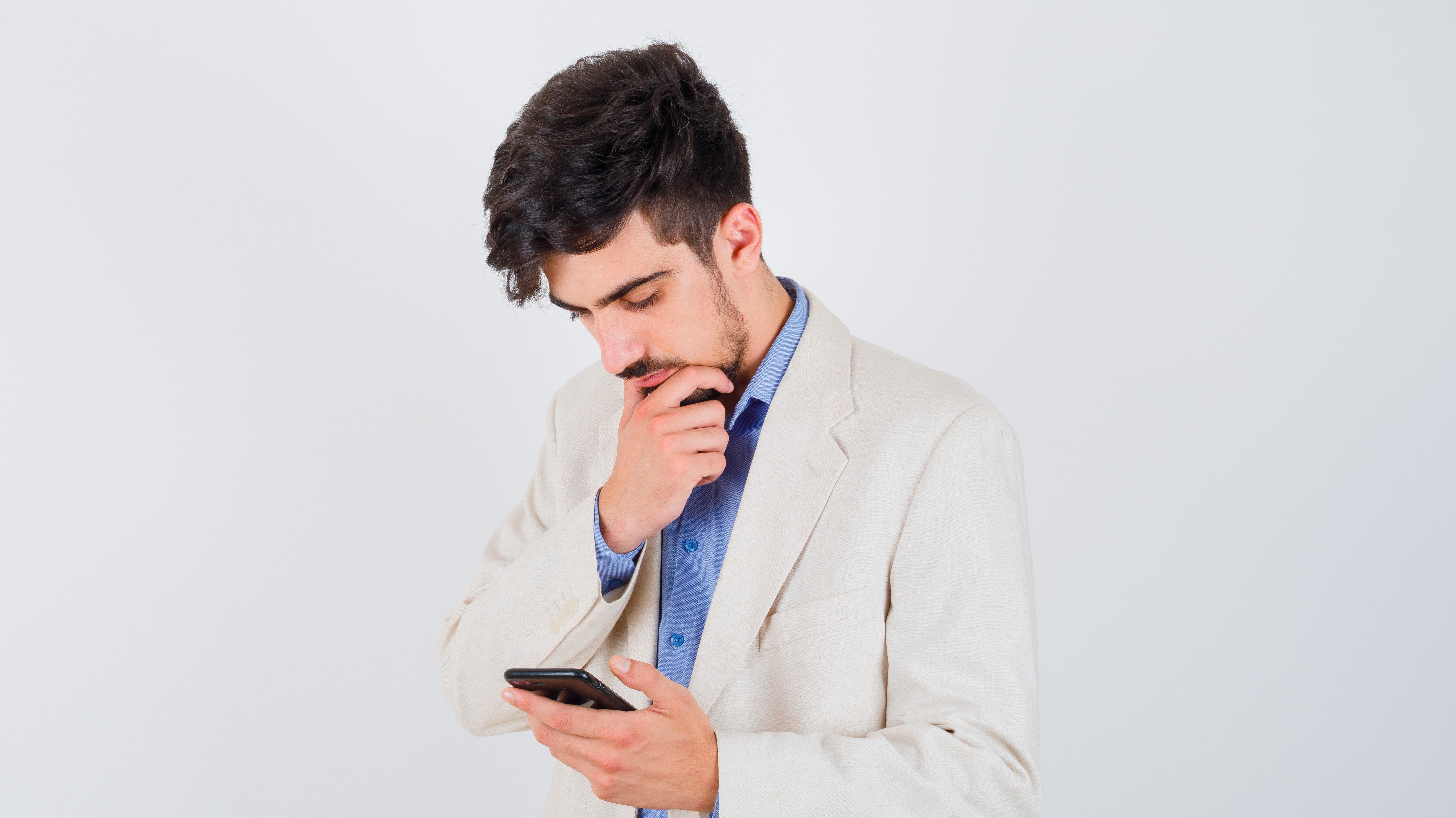 young-man-blue-t-shirt-white-suit-jacket-holding-smartphone-standing-thinking-pose-looking-pensive.jpg